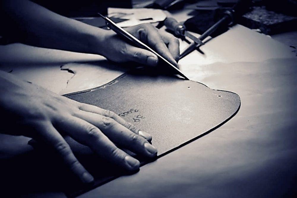 Le mani di un artigiano tagliano con il trincetto un pezzo di pelle sul modello di carta